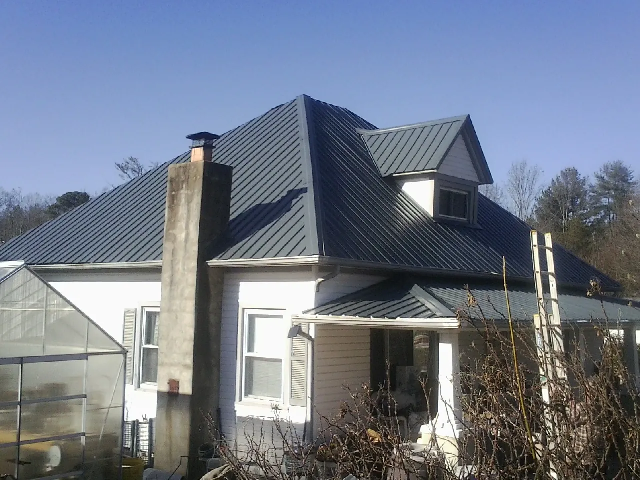 Dark blue standing seam metal roof on a white farmhouse with dormer — Slate & Tile Roof Repair by Roofing Brothers in Hanson